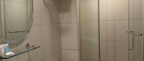 A modern bathroom with a glass-enclosed shower, a round mirror, and a white sink.
