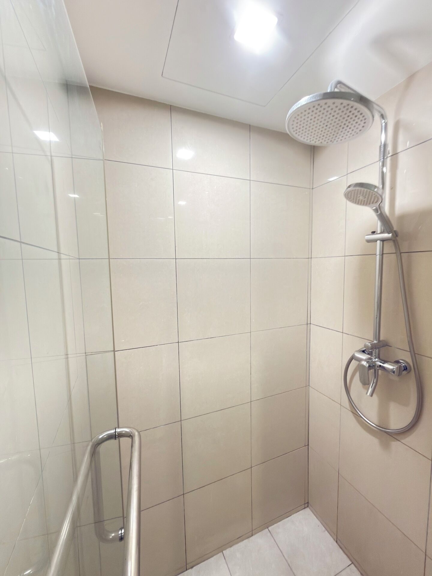 Baño en esquina con ducha, paredes revestidas de azulejos y barandilla.