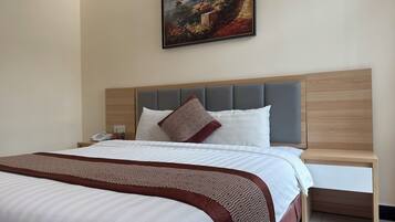 Una habitación de hotel con una cama, una mesita de noche con un teléfono, una lámpara de noche y un cuadro en la pared.