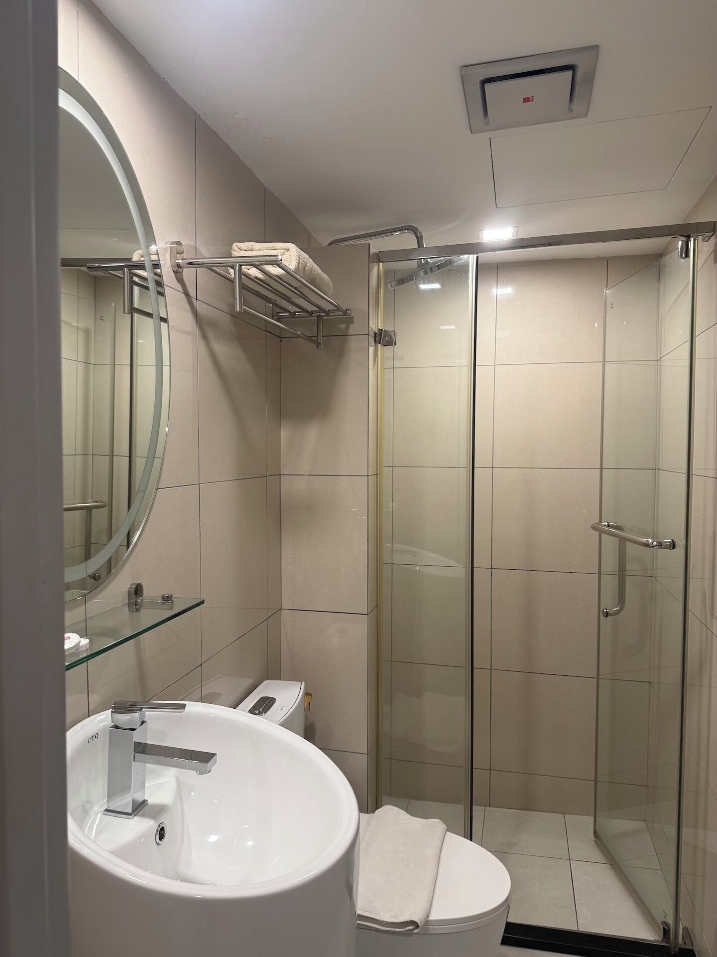 A modern bathroom with a glass-enclosed shower, a round mirror, and a white sink.