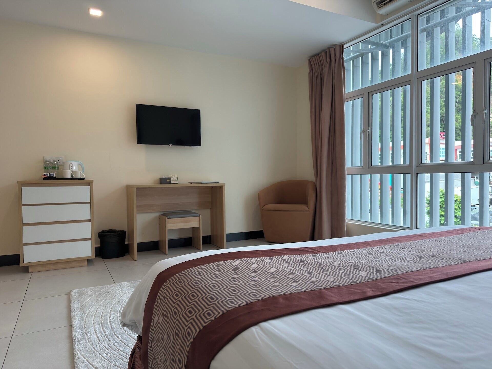 Habitación de hotel con cama, escritorio, silla, televisor y ventana con cortinas.