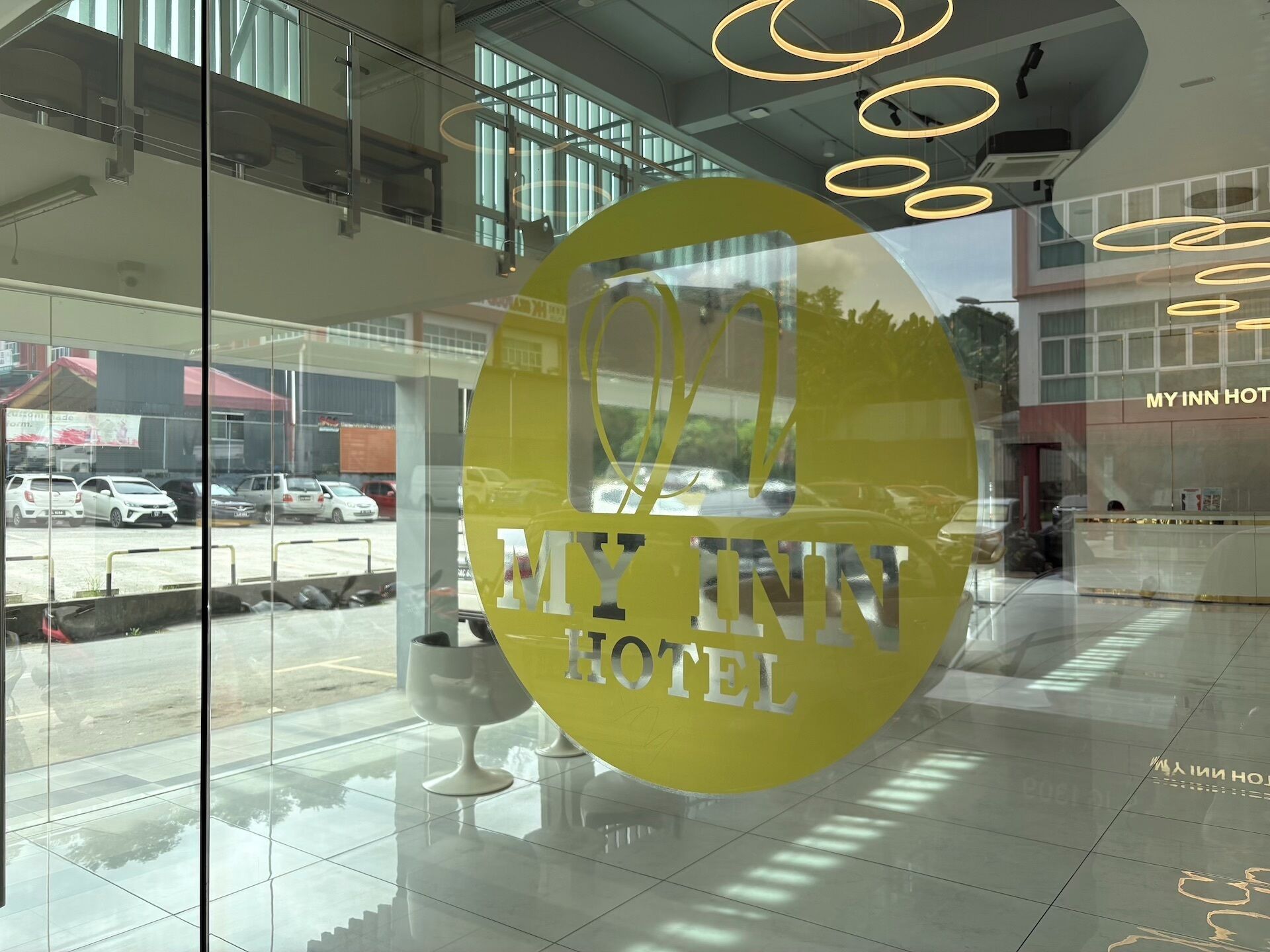 A hotel reception area with a glass facade, modern interior design, and a visible parking lot outside.