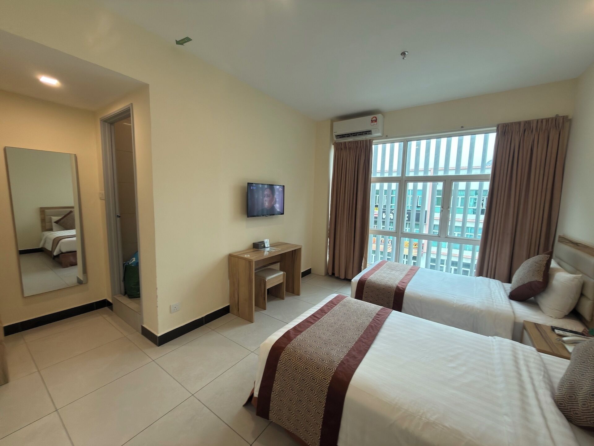 Habitación de hotel con dos camas, un televisor, un escritorio y un ventanal grande con cortinas.