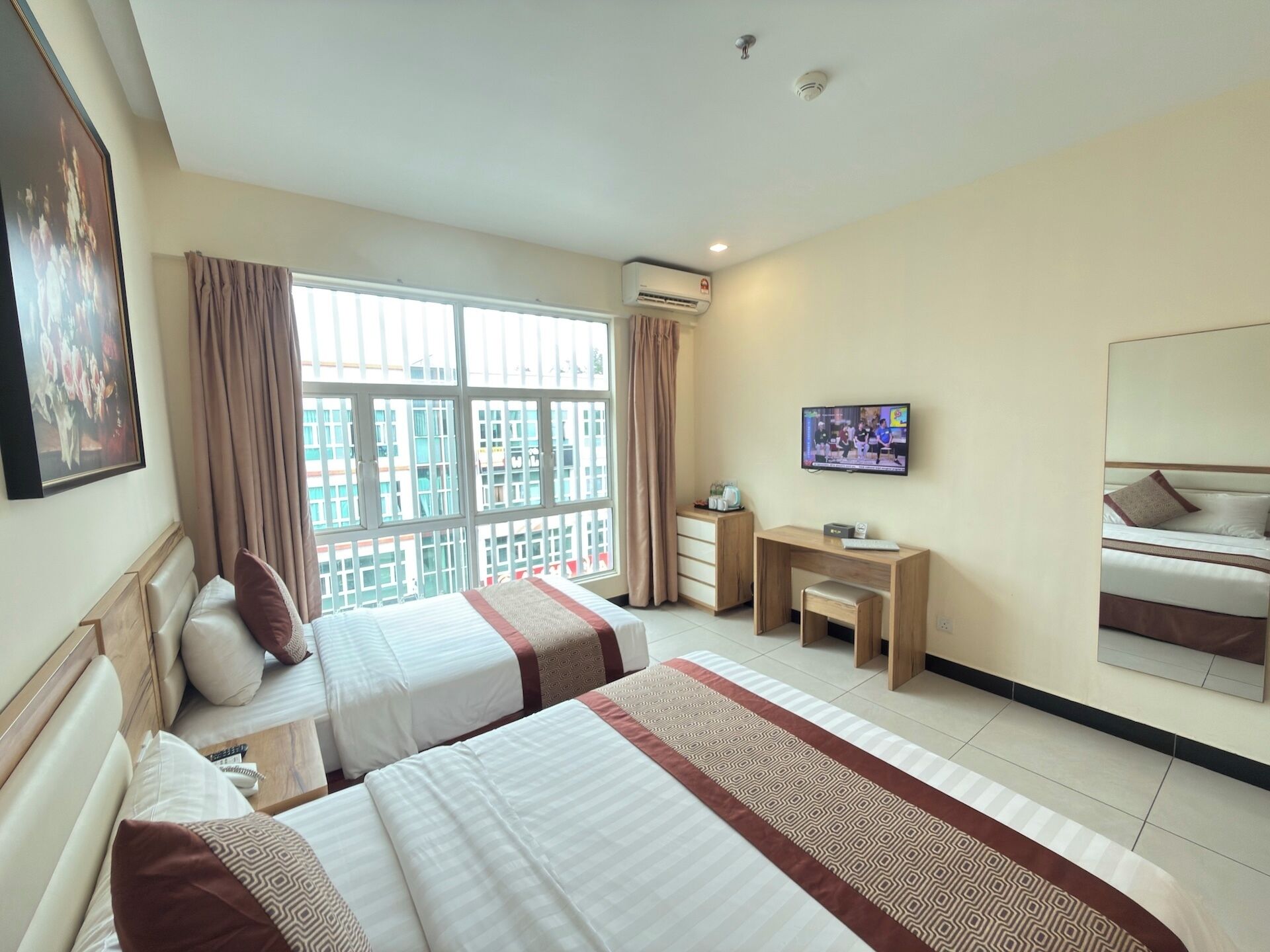 Habitación de hotel con dos camas, un escritorio, televisión y balcón con vistas.