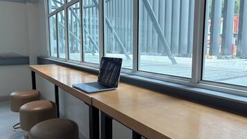 Un espacio de trabajo moderno con una computadora portátil sobre una mesa de madera, ventanas amplias y vistas a un área exterior.