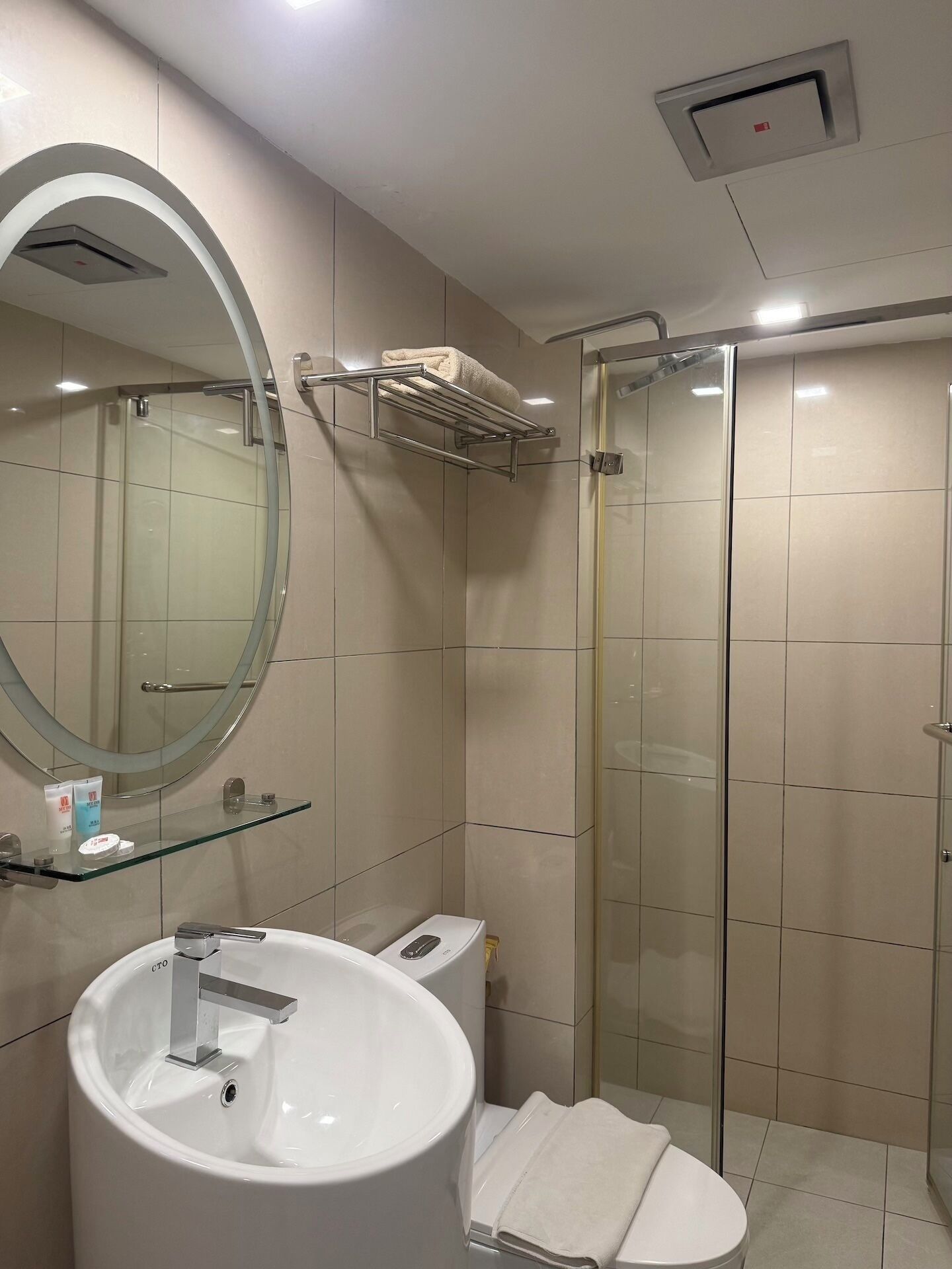 Ein modernes Badezimmer mit großem Waschbecken, Spiegel, Duschkabine aus Glas und einem Handtuchhalter.