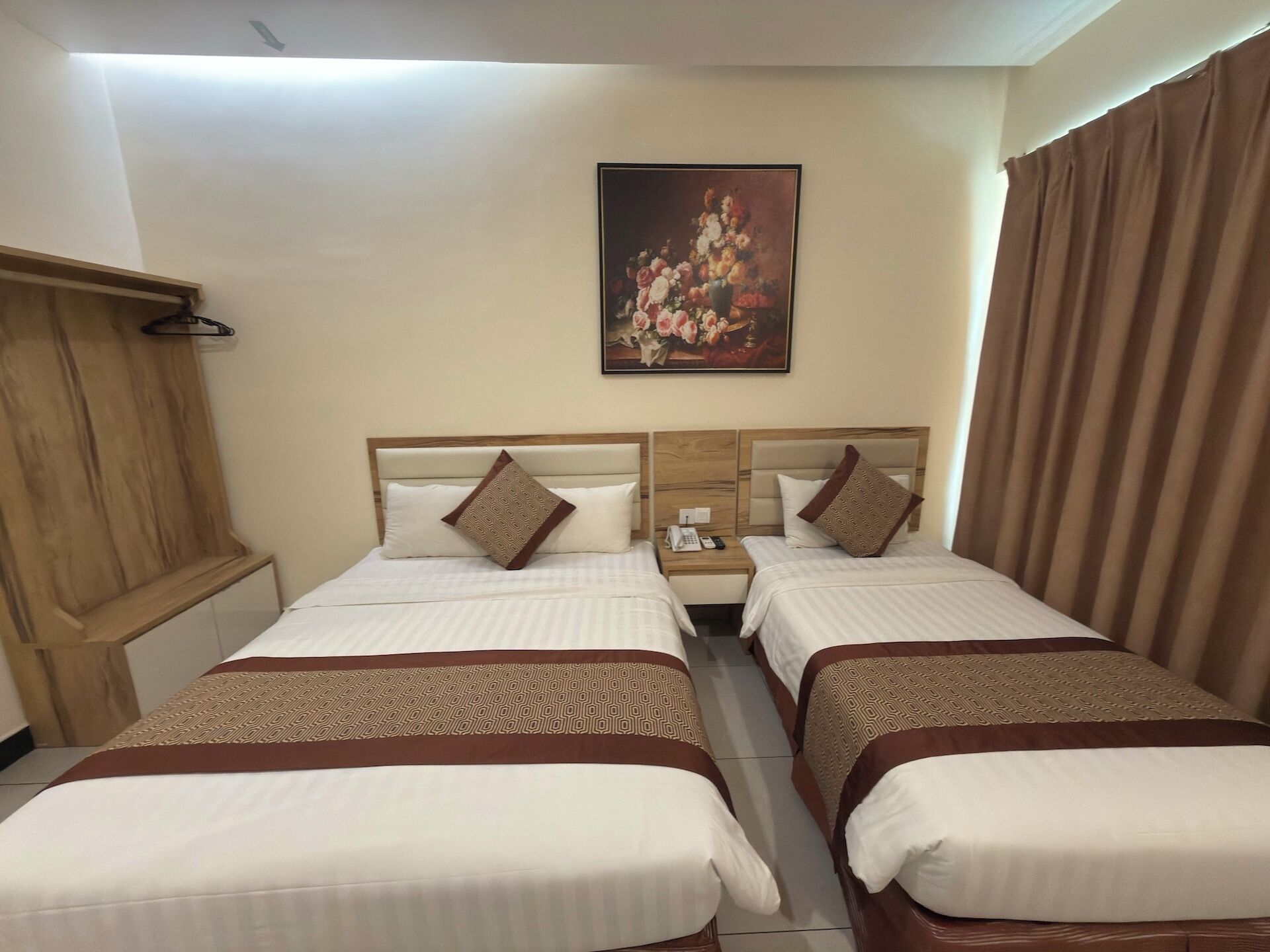 A hotel room with two beds, a painting on the wall, and a wooden wardrobe.
