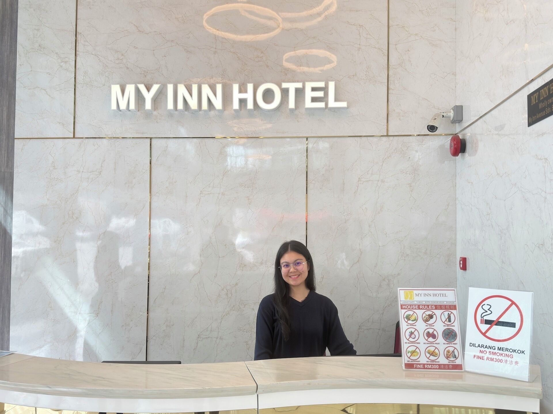 A reception desk at MY INN HOTEL with a marble wall background, a sign listing house rules, and a no-smoking sign.