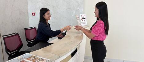 Una recepción de hotel con pared de mármol, un letrero de prohibido fumar y una recepcionista.