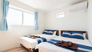 Ein Hotelzimmer mit zwei Betten, einem Fenster mit Vorhängen, einer kleinen Wand-Klimaanlage und Holzboden.