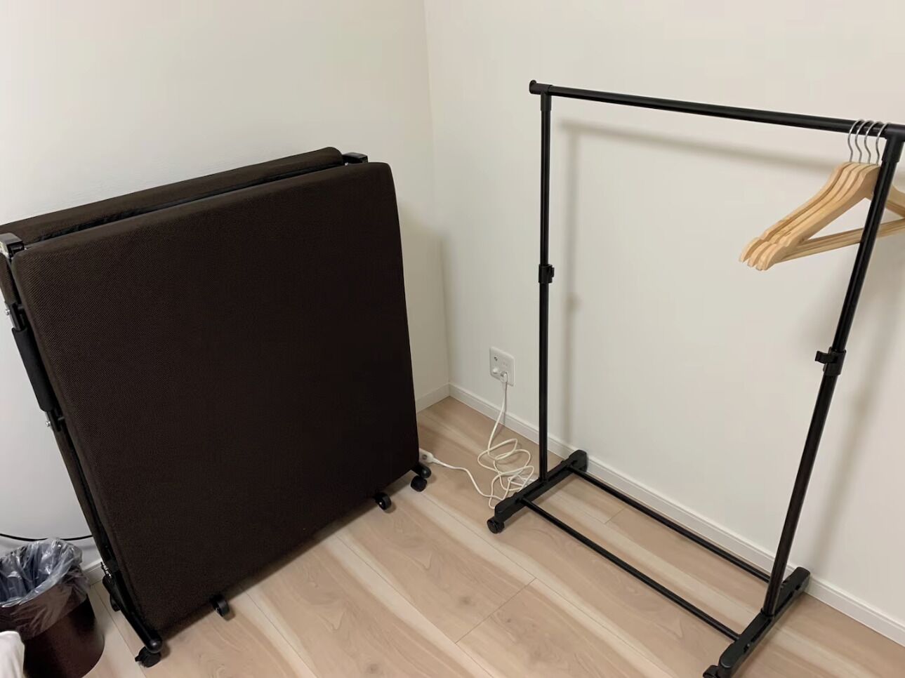 A room with a black folding screen, a black metal rack with a wooden hanger, and a white electrical outlet on the wall.