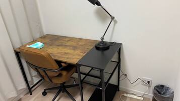 A desk with a chair, a lamp, a trash bin, and a power strip.