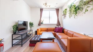 Ein modernes Wohnzimmer mit einem Ecksofa, einem Flachbildfernseher, einem Couchtisch und einem Feuerlöscher.