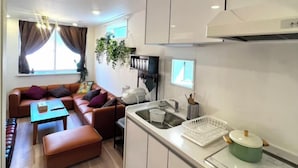 Ein kompakter Wohnraum mit Küchenzeile, einer Couch, einem Esstisch und einem fenster mit Vorhängen.