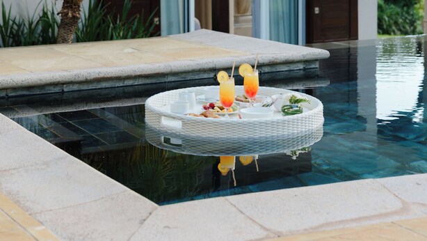 En pool med ett runt bord, en palm och en byggnad med en pergola.