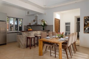 A modern kitchen with a central island, dining area with wooden table and chairs, and a view of the outdoors. - Terrace 4-Bedroom Villa / Infinity Pool & Tropical Garden (Bel Ombre)