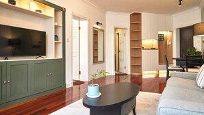 Un salon avec un téléviseur à écran plat, une table basse ornée d’une plante, un canapé et une bibliothèque.