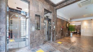 A hotel lobby with a reception desk, a glass elevator, and a potted plant. - Hasen Nabeeya Hotel (Siheung)