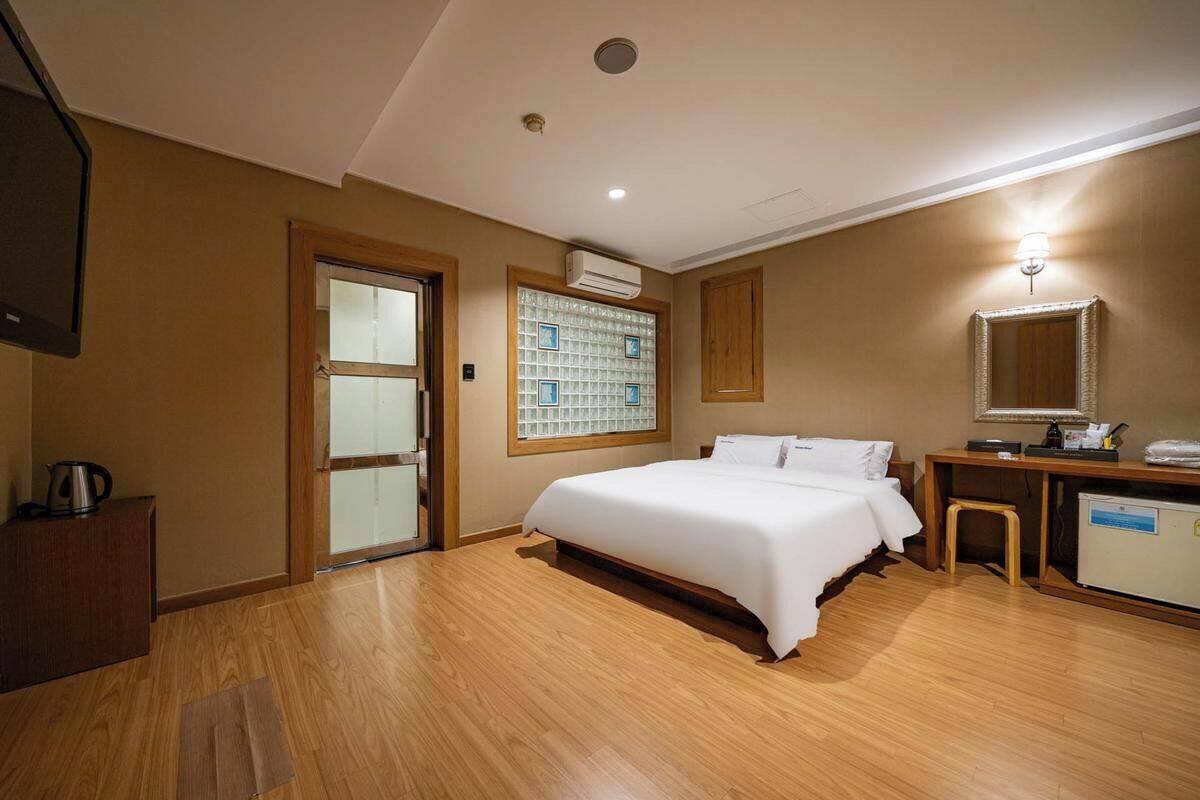 A hotel room with a bed, a desk, a chair, a television, and an air conditioning unit.