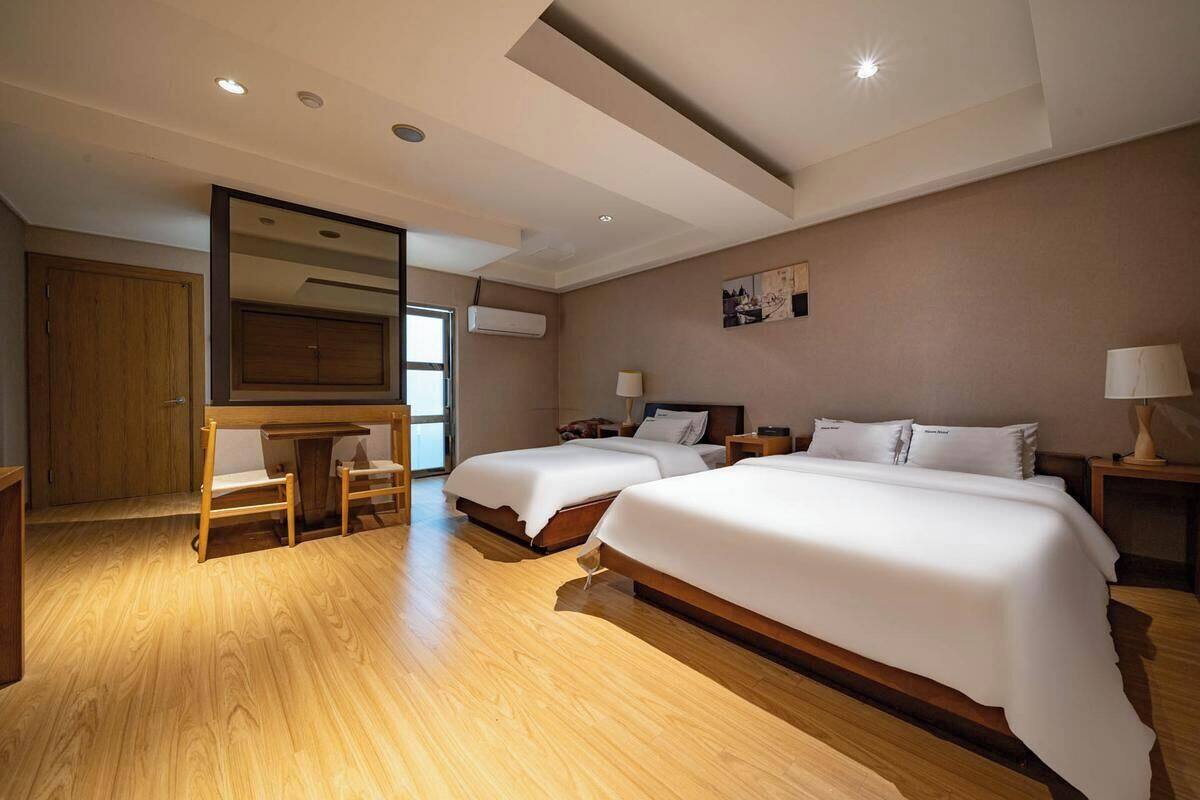A hotel room with two beds, a desk, a chair, a wardrobe, and a large mirror.