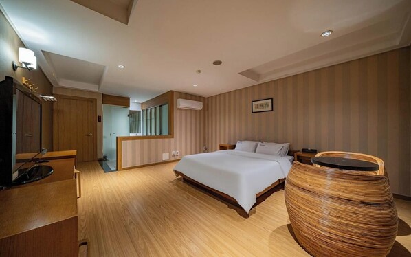 A modern hotel room with a wooden floor, a large bed, a television, a bedside table, and a wicker side table. - Hasen Nabeeya Hotel (Siheung)