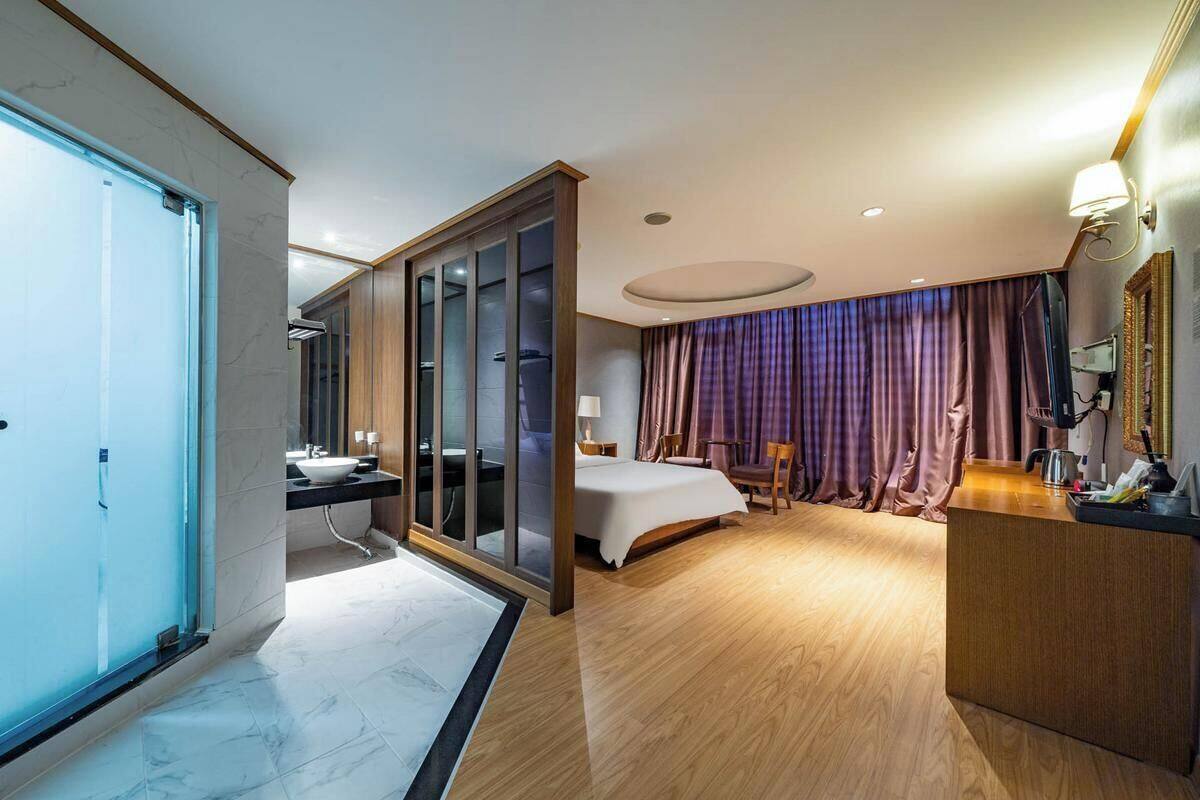 A hotel room with a glass door, a bed, a desk, and a bathroom.