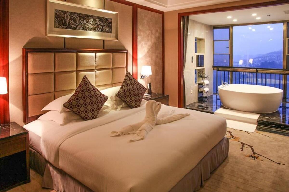 Une chambre d’hôtel avec un grand lit, une baignoire et un balcon offrant une vue sur la ville.
