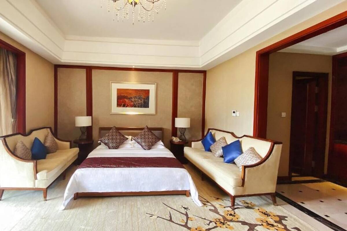 Une chambre d’hôtel avec un grand lit, deux canapés, un lustre et un tableau au mur.