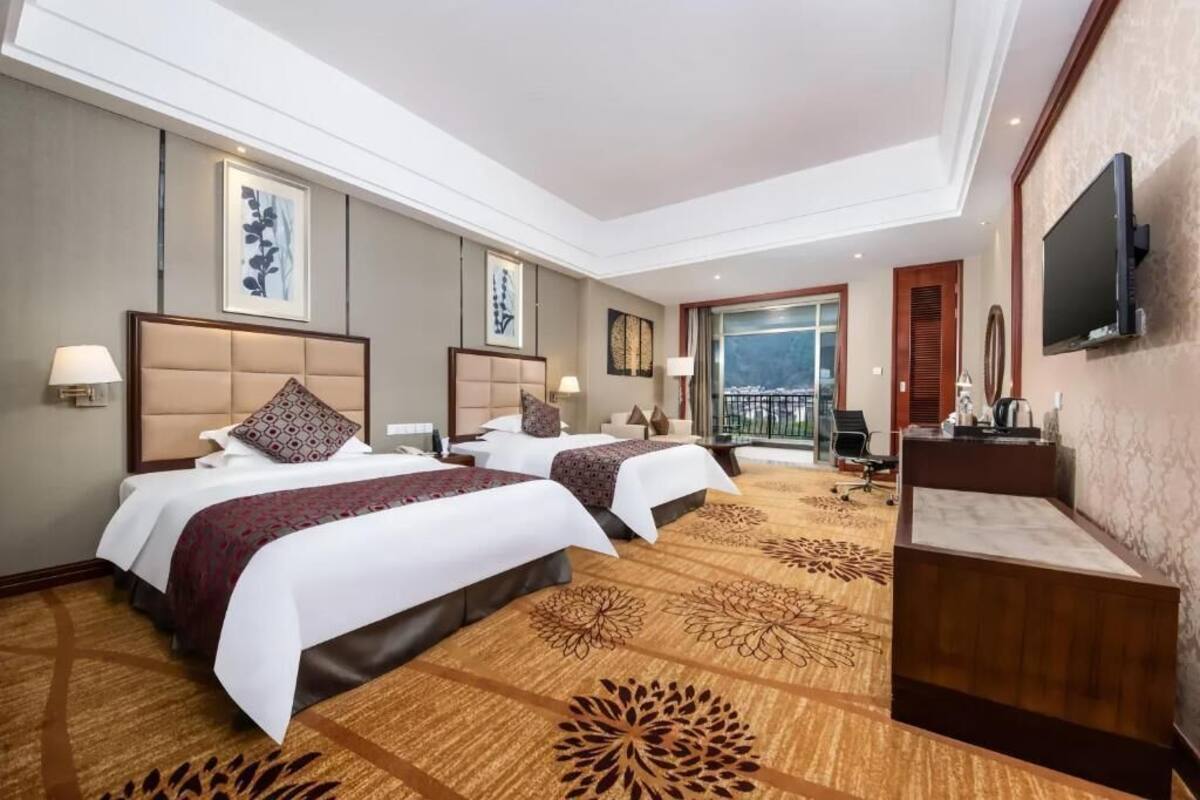Une chambre d’hôtel avec deux lits, un bureau, une télévision et un balcon avec vue.