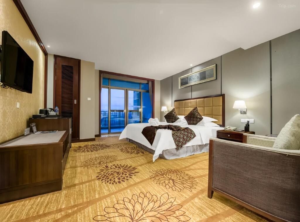 Une chambre d’hôtel équipée d’un lit, d’un bureau, d’une chaise, d’une télévision et d’une porte donnant sur un balcon.