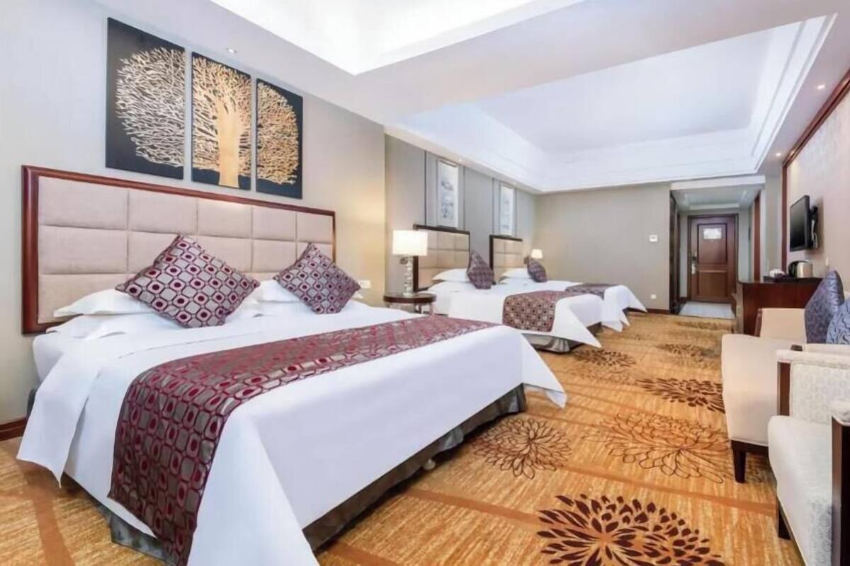 Une chambre d’hôtel avec trois lits, un canapé, une télévision et des œuvres d’art accrochées aux murs.