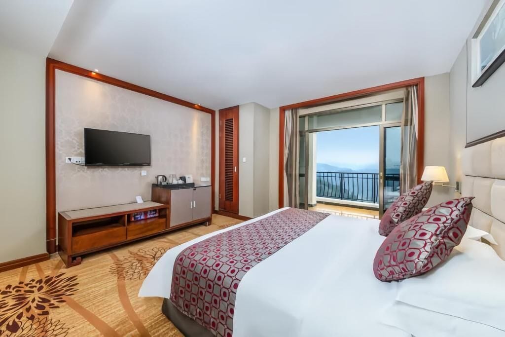 A hotel room with a bed, a TV, a balcony, and a view of the sky.