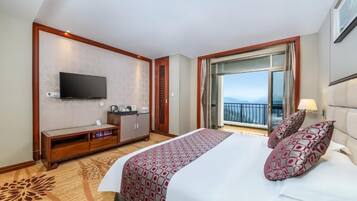 A hotel room with a bed, a TV, a balcony, and a view of the sky.