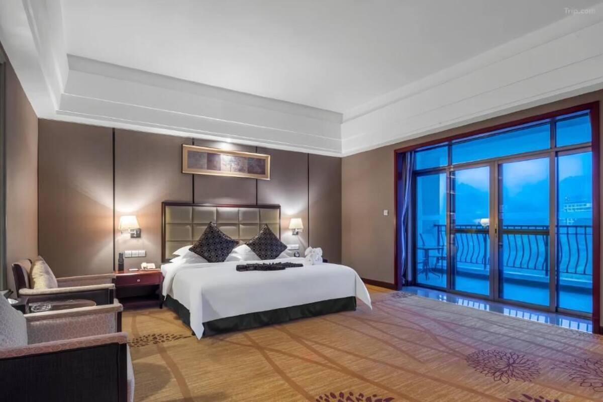 Une chambre d’hôtel avec un grand lit, une table de chevet, une chaise, une fenêtre donnant sur un beau paysage et un plafond doté d’un éclairage encastré.