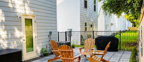 Eine Terrasse mit Adirondack-Stühlen, einem Grill und einer kleinen solarbetriebenen Beleuchtung.