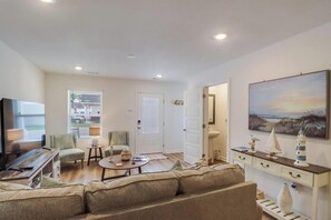 A living room with a sofa, coffee table, and a television. There is a door leading to another room and a window with a view of the outside. - Cozy Gulfport Beach Home - Seahorse Harbor (Gulfport)