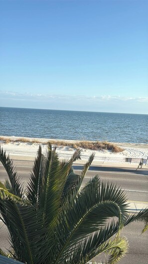 Strandblick mit Palmen im Vordergrund und blauem Himmel.