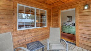A wooden cabin interior with a large window, two wicker chairs, a small table, and a green dresser. - Serene 4-bedroom  spacious house in Pagosa Springs perfect for your getaway. (Pagosa Springs)