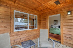 A wooden cabin interior with a large window, two wicker chairs, a small table, and a green dresser. - Serene 4-bedroom  spacious house in Pagosa Springs perfect for your getaway. (Pagosa Springs)