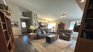 A spacious living room with a large brown leather sofa, a wooden coffee table, and a rug. There is a kitchen in the background with wooden cabinets and a dining area. - Serene 4-bedroom  spacious house in Pagosa Springs perfect for your getaway. (Pagosa Springs)