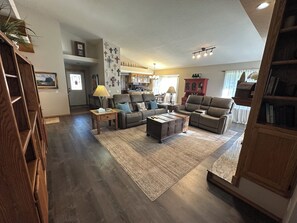 A spacious living room with a large brown leather sofa, a wooden coffee table, and a rug. There is a kitchen in the background with wooden cabinets and a dining area. - Serene 4-bedroom  spacious house in Pagosa Springs perfect for your getaway. (Pagosa Springs)