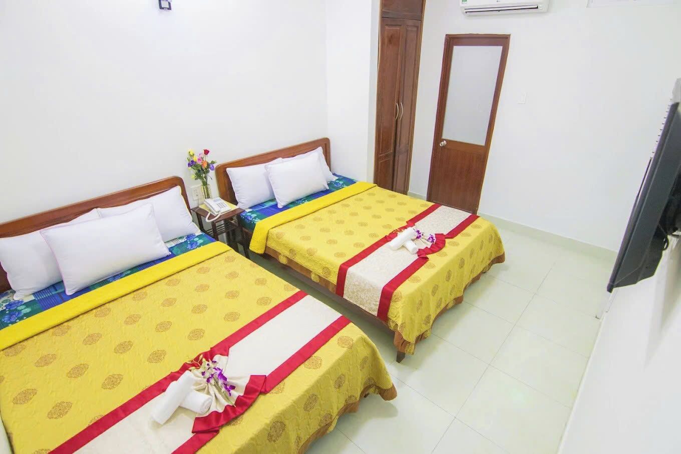 A hotel room with two beds, a wooden wardrobe, a mirror, and a television.