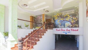 Una scala conduce all'ingresso di un edificio, con un cartello che riporta la scritta 'Kinh Chao Zuý Khách MAX 2M'.