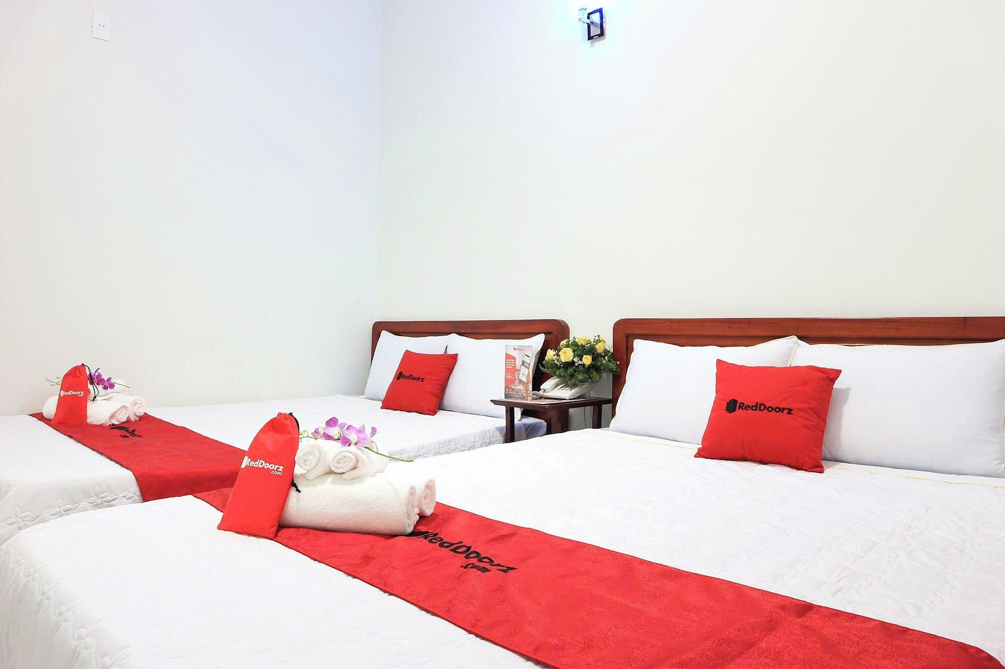 A hotel room with two beds, each with white linens and red accents, including towels and pillows.