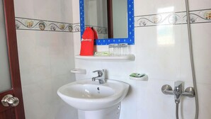 Un bagno con un lavandino bianco, uno specchio, una doccia e una borsa rossa su uno scaffale.