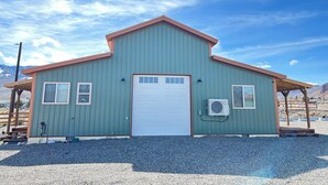 A single-story building with a garage door, two windows, and an air conditioning unit mounted on the wall. - Relaxing Rustic Barndominium with Mountain View’s in Challis Idaho (Challis)