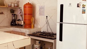 A kitchen with a white refrigerator, a gas stove, a shelf with kitchenware, and a sign on the wall. - Bossa Nova Home - a private house 5 minutes from the beach with Brazilian style! (Barra dos Coqueiros)
