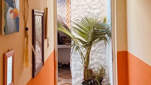 A hallway with a door leading to a room, decorated with wall art, a woven wall hanging, and potted plants. - Bossa Nova Home - a private house 5 minutes from the beach with Brazilian style! (Barra dos Coqueiros)