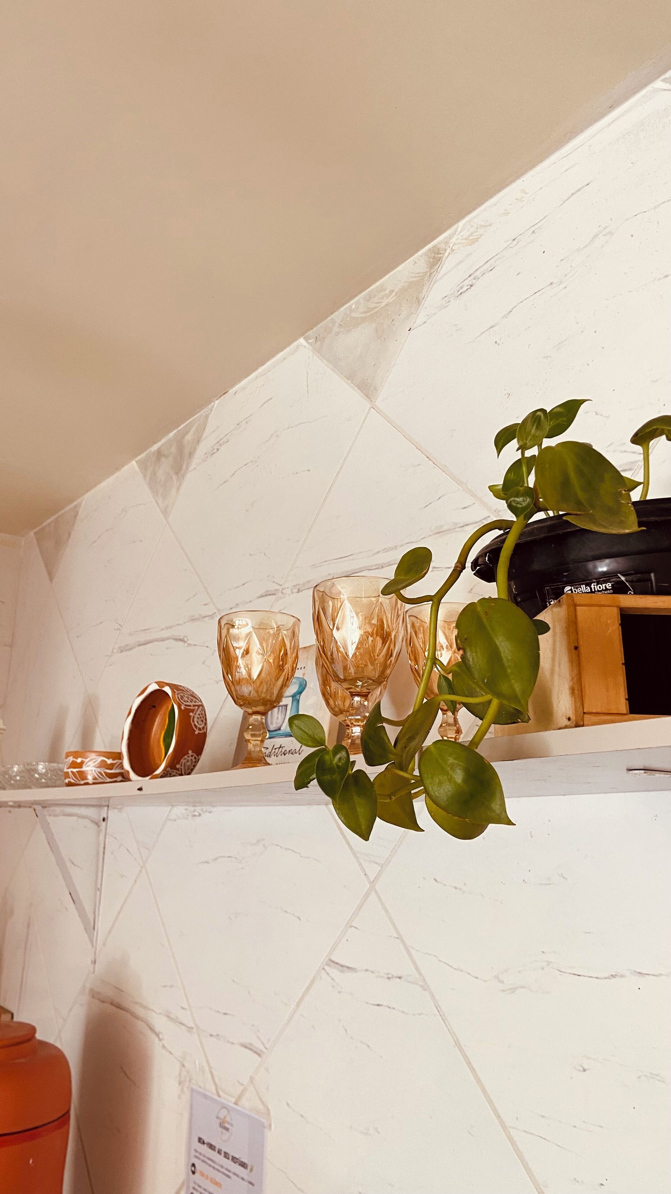 A kitchen with white marble tiles, a shelf with decorative items, and a potted plant.