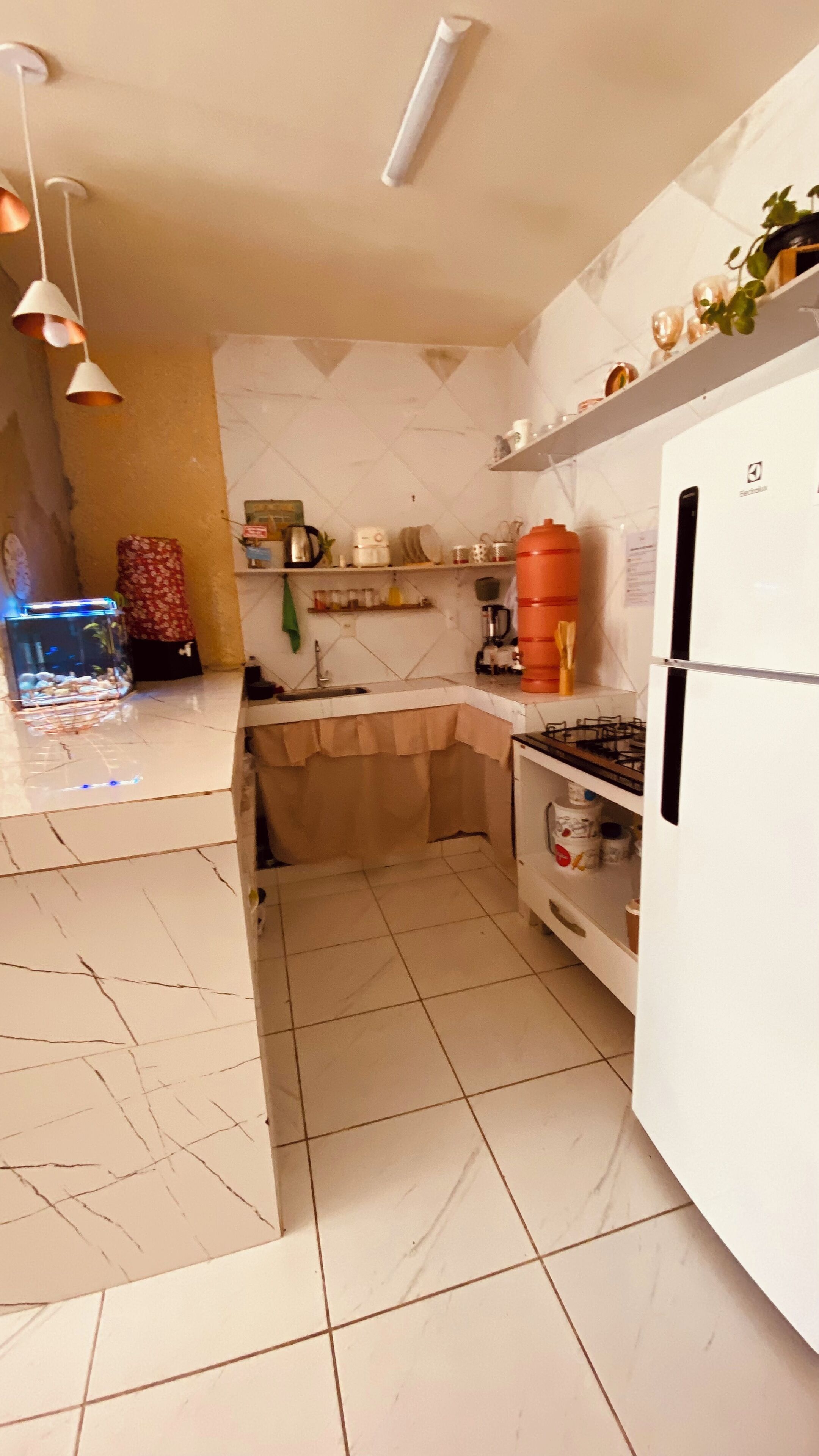 Uma cozinha compacta com geladeira branca, pia, fogão e um aquário.